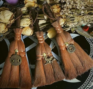 Macro detail of three mini wicca altar brooms with bronze charms and wooden handles