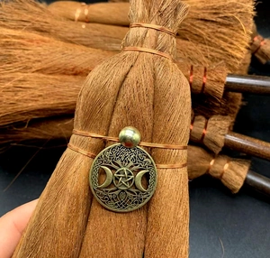 Macro detail of wicca broom charm featuring bronze triple moon pentagram and crystal