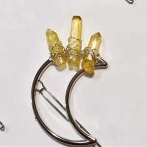 Detail of silver moon hair clip with hand-wrapped yellow crystal stones on white background