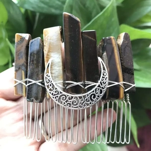 Detail of handmade tiger eye stone hair comb with silver crescent moon held in hand