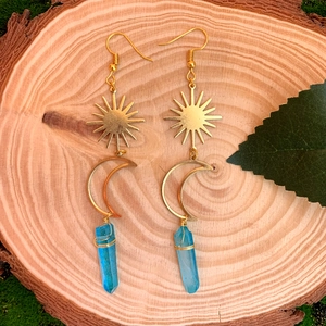 Détail de boucles d'oreilles soleil et lune avec cristaux bleus sur bois naturel