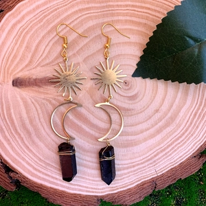 Détail boucles d'oreilles soleil lune dorées avec cristal noir sur fond de bois