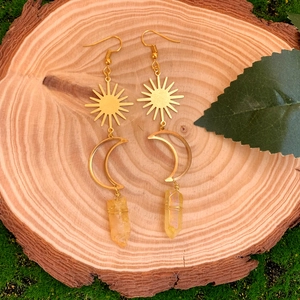 Détail de boucles d'oreilles soleil et lune avec cristaux naturels sur tranche de bois