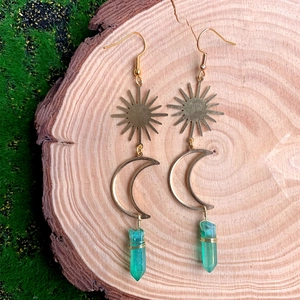 Détail de boucles d'oreilles lune et soleil avec cristal vert sur fond de mousse naturelle