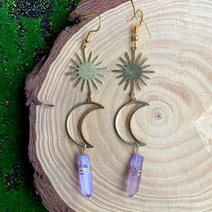Détail de boucles d'oreilles soleil et lune avec cristal violet sur bois et mousse