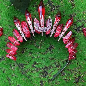 Detail view of a gothic crown with red crystals and silver moon on a mossy background