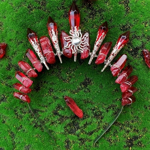Red crystal crown headband with silver sun ornament and spikes on green moss background