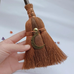 Detail of wicca mini broom with bronze moon pendant and natural fibers held in hand