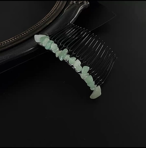 Detailed close-up of 20-tooth black metal hair comb with raw green crystal stones