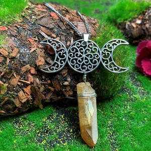 Macro view of handmade triple moon goddess necklace with raw crystal point on mossy bark