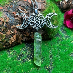Macro detail of Triple Moon Goddess necklace with raw green crystal on mossy bark