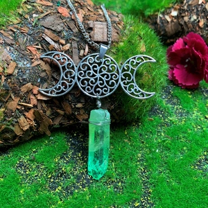 Macro detail of triple moon goddess pendant with green crystal on mossy bark background