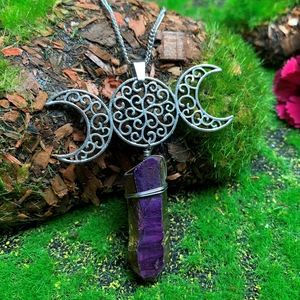 Macro shot of silver triple moon pendant with purple crystal on mossy wood background