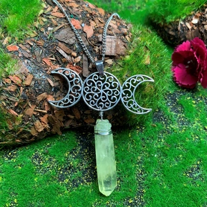 Macro detail of triple goddess moon pendant with green crystal column on tree bark
