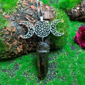 Detailed close-up of triple moon goddess necklace with crystal point on mossy tree bark