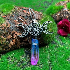 Close-up of handmade triple moon necklace with colorful crystal on mossy wood