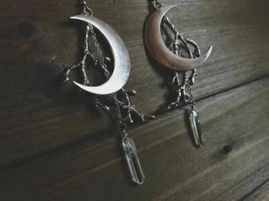 Detailed close-up of triple moon crystal earrings on a rustic wood background