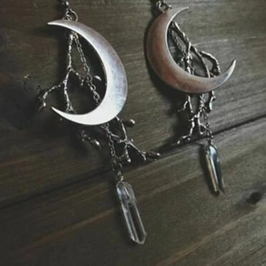 Gothic silver-toned moon and crystal column drop earrings on a rustic wood background