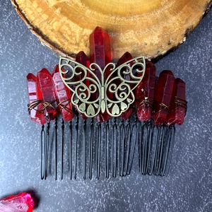 Detail of dark red crystal quartz hair comb with bronze butterfly on wood base