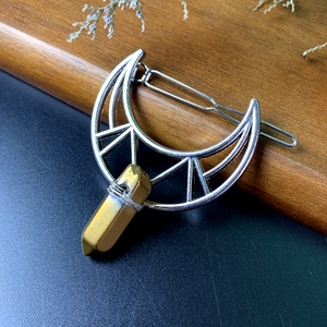 Macro view of silver moon hair clip with golden crystal on a dark wood background