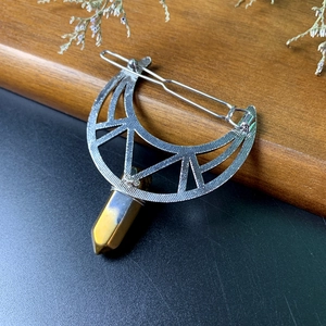 Detailed view of silver moon hair clip with tiger eye crystal prism on wood background