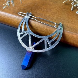 Macro shot of silver crescent moon hair clip with blue crystal prism on wood texture