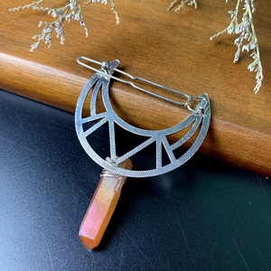 Detailed view of handmade moon-shaped hair clip with natural orange crystal and wire wrap