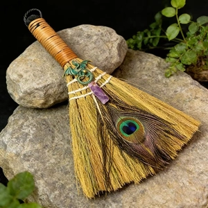 Handmade altar broom with purple crystal, dragon charm, and peacock feather on grey rock