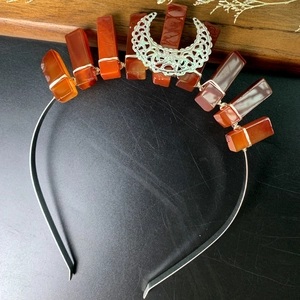 Detail of silver crown headband featuring rectangular orange stones and a crescent ornament