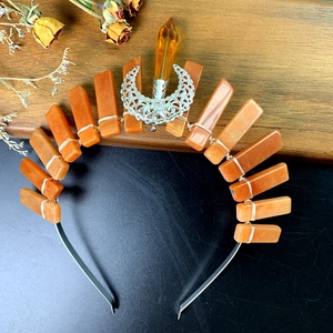 Detail of handmade orange crystal crown with silver moon on a rustic wooden surface