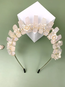 Détail du serre-tête avec cristaux roses, fleurs blanches et perles sur fond vert
