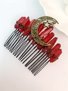 Detail view of red raw crystal hair comb with bronze moon and star charm on white background