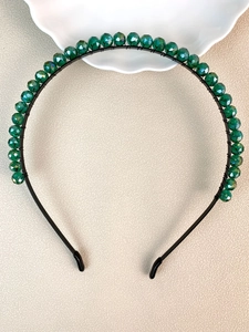 Macro detail of handmade headband with deep green faceted crystals on a black frame