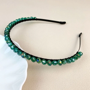 Elegant thin black metal headband with green faceted crystals on a textured background