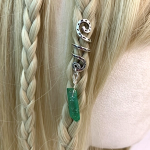 Detail of vintage silver hair coil with green crystal pendant on braided hair