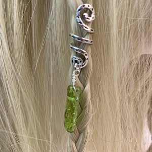 Close-up of a silver spiral hair ring with green crystal stone pendant on braided hair