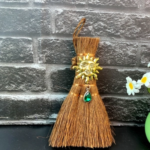 Close-up of mini Wicca broom with golden sun charm and green crystal droplet pendant