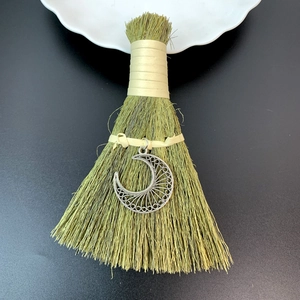 Close-up of small straw broom with silver crescent moon pendant on black background