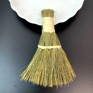 Macro shot of handmade mini straw broom featuring golden moon pendant on black background