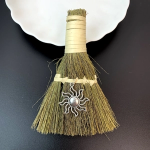 Detailed close-up of decorative straw broom with silver sun pendant and leather handle