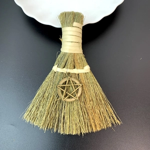 Detailed view of handmade straw besom with vintage bronze pentagram charm on black background