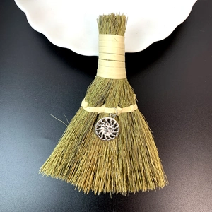 Detailed close-up of handmade straw broom ornament with a sun face charm on black surface