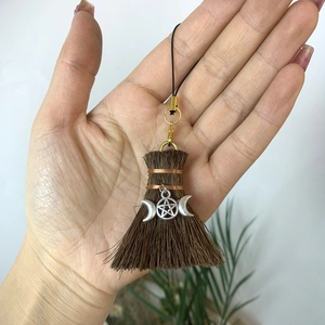 Macro detail of witchy broom pendant featuring pentagram and triple moon symbols