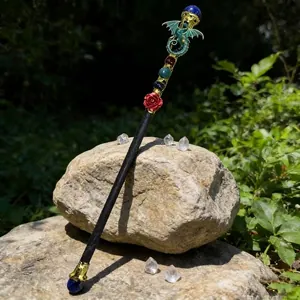 Close-up of crystal magic wand with a green dragon, red rose, and colorful gems on rocks