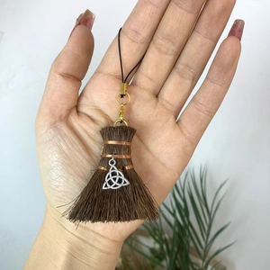 Handheld view of a brown wizard broom pendant with silver Celtic knot and metal clasp