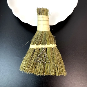 Detail view of mini decorative straw broom with a silver Triquetra knot metal charm