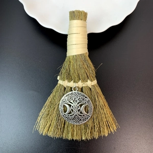 Close-up of small decorative witch broom with silver pentagram pendant on black background