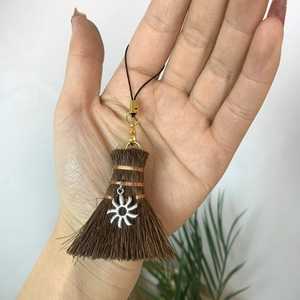 Close-up of handmade broom charm with sun metal pendant and black braided lanyard decor