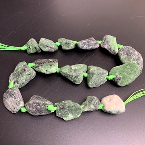 Macro shot of natural unpolished ruby zoisite raw stones on a green necklace string
