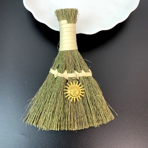 Macro detail of decorative straw broom featuring a golden sun pendant on dark background